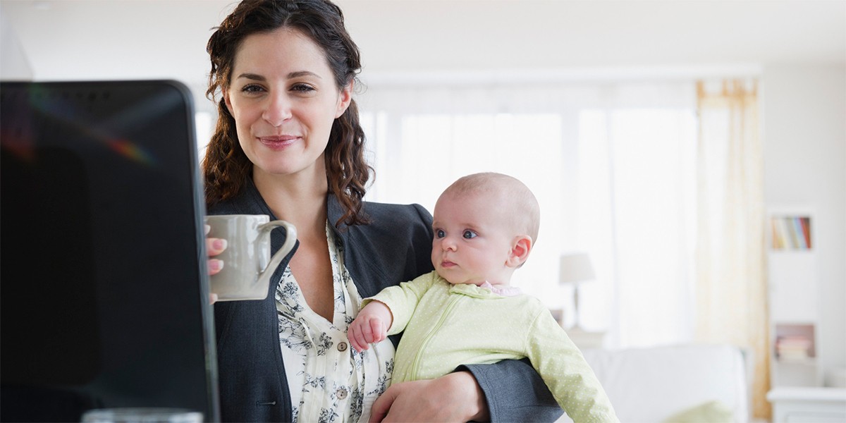 Mãe conciliando o trabalho com a maternidade, segurando o filho em seu colo enquanto toma café na empresa